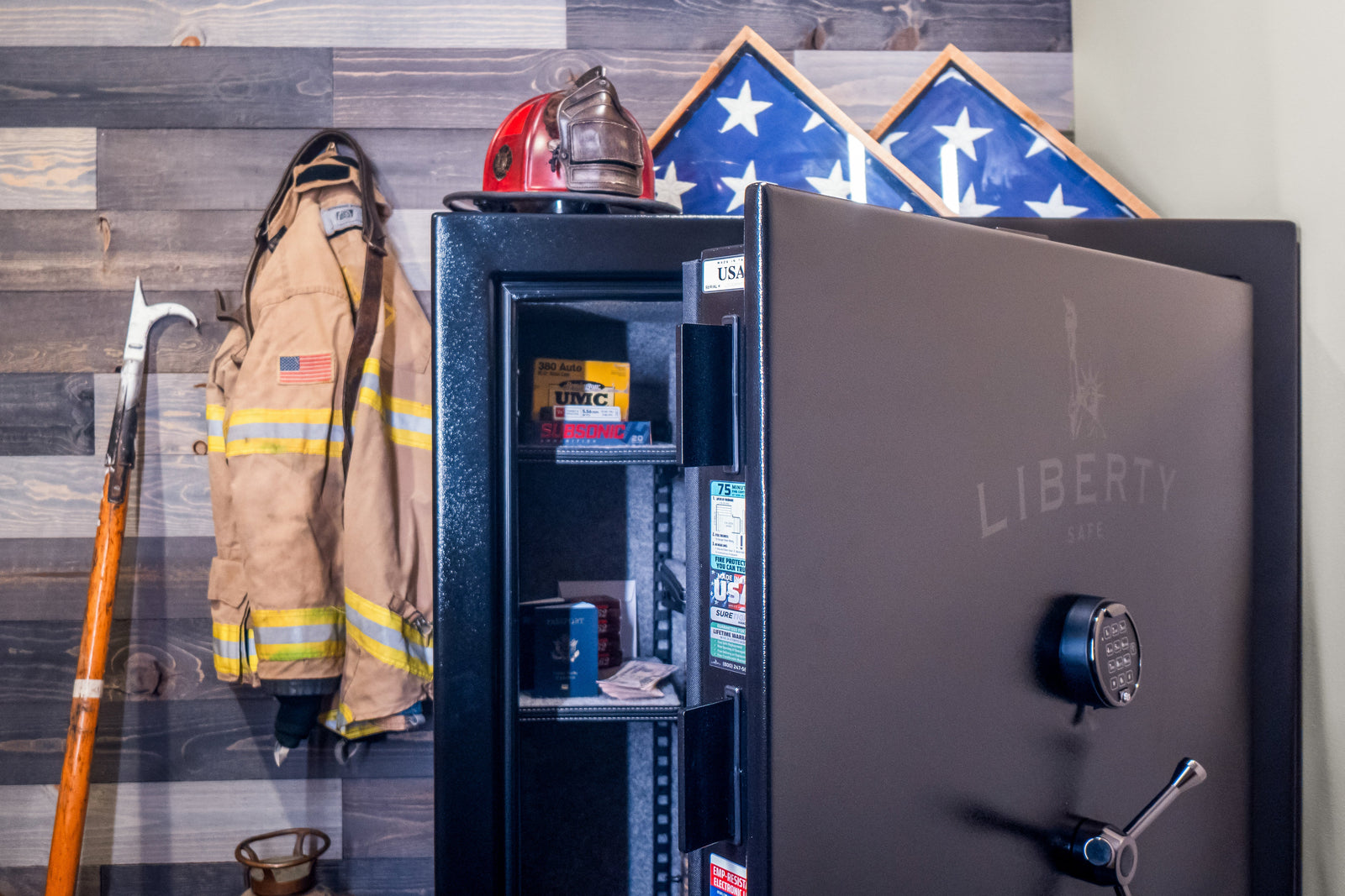 Open Liberty gun safe with electronic keypad lock storing ammunition, passports, and cash beside firefighter gear and folded American flags